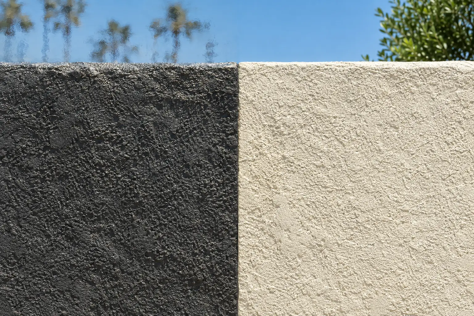 Dark charcoal stucco wall beside a pale cream stucco wall in direct sun
